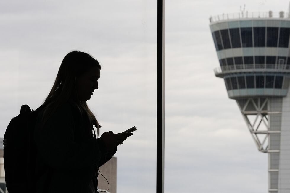 FILE - A traveler with a smartphone walks past an air traffic control tower at Philadelphia...